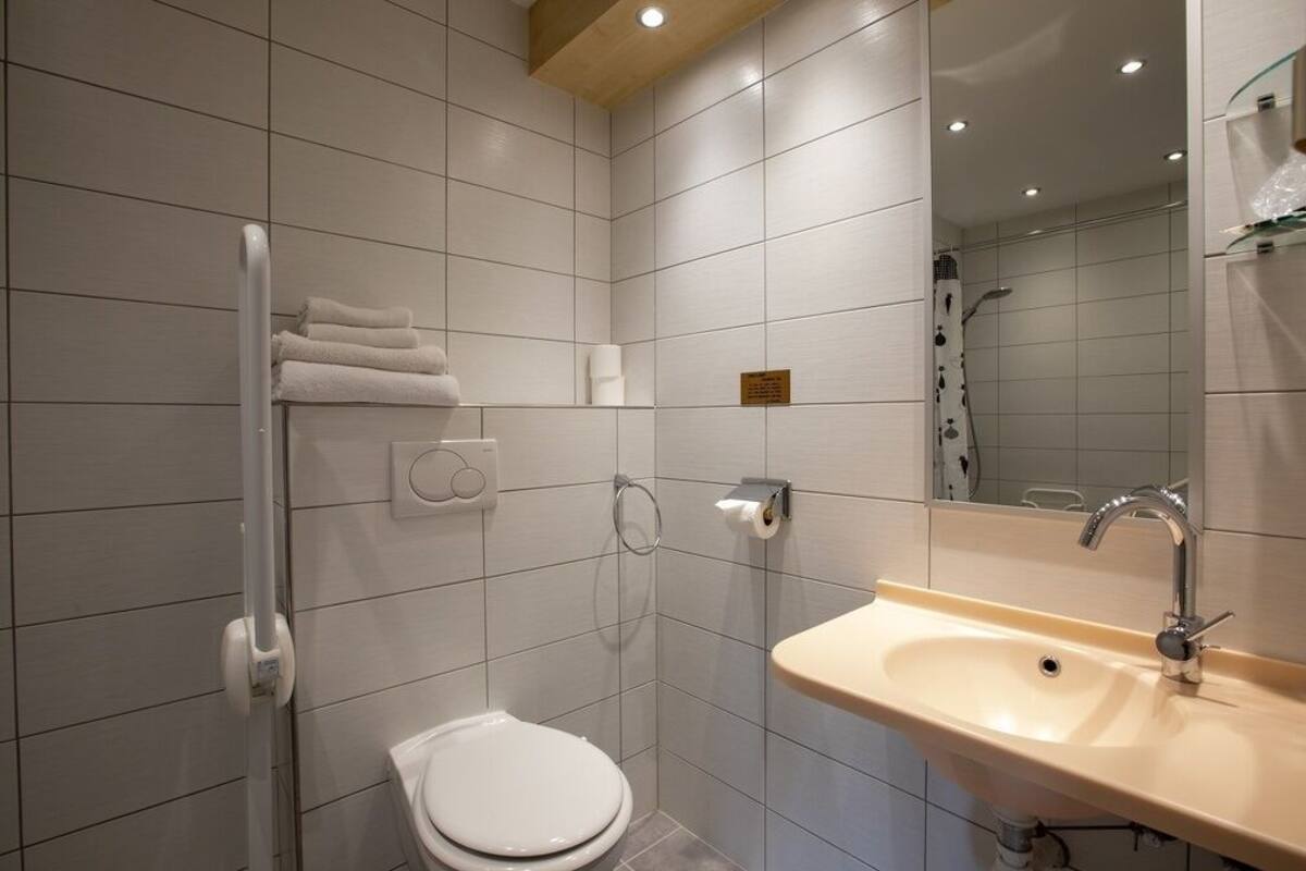Un baño moderno con inodoro blanco, lavabo con espejo y toallero.