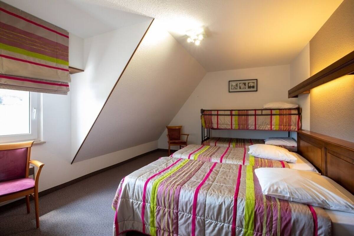 Un dormitorio con una cama litera, una silla, una ventana con persianas y una lámpara en el techo.