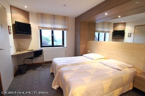 A hotel room with two beds, a desk with a computer, a television, and a window with a view of greenery. - Hotel Restaurant & Spa Au Tilleul (Labaroche)
