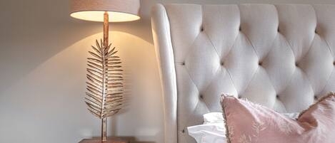 A bedroom with a tufted headboard, a bedside lamp with a leaf-shaped base, and a white nightstand.