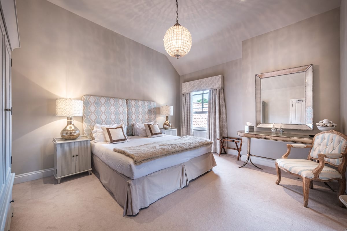 A bedroom with a large bed, bedside tables, a dresser, a vanity with a mirror, and a chair.