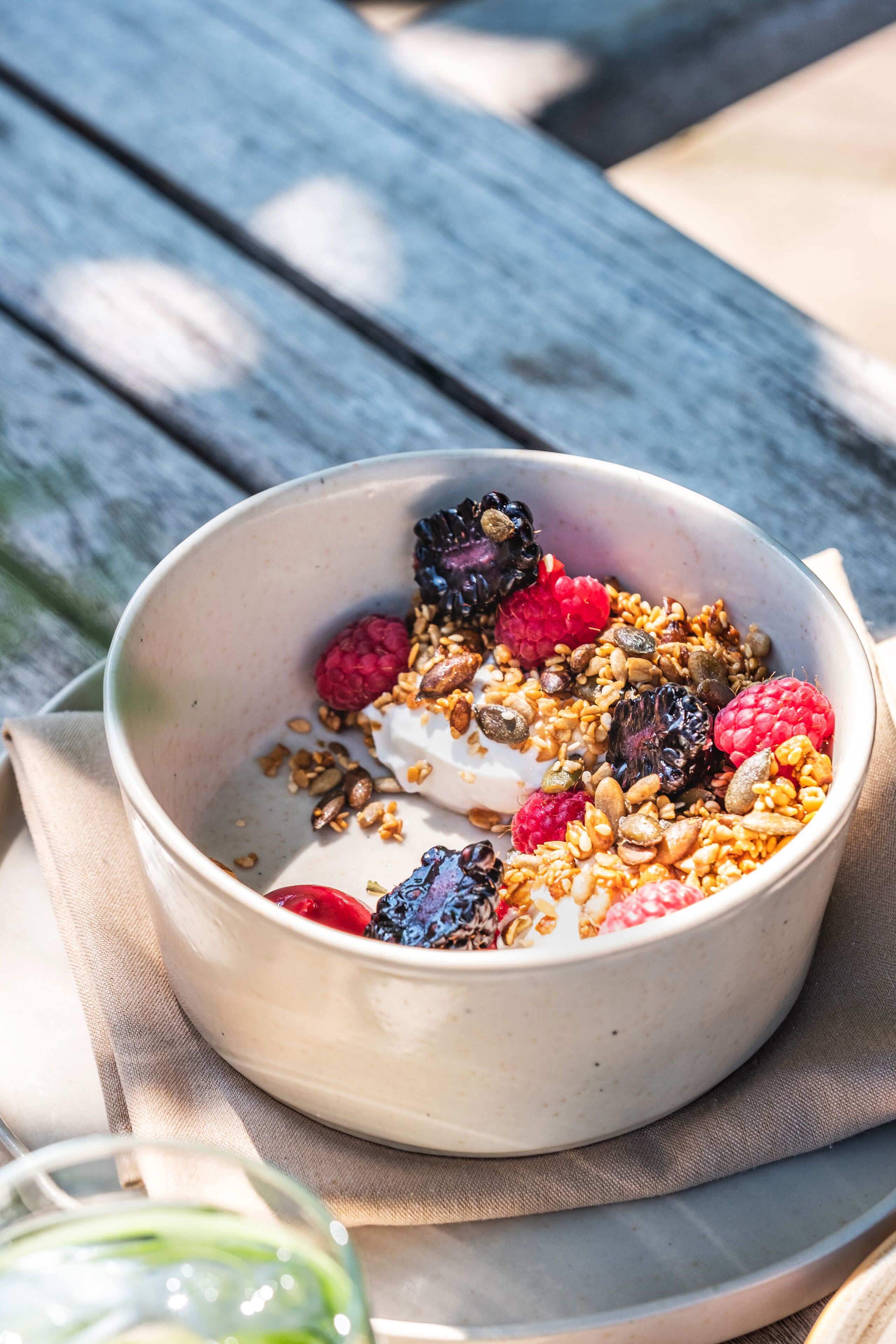 A bowl of yogurt with granola and berries on a beige napkin.