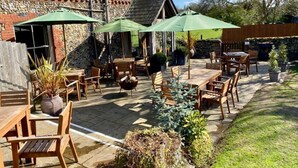 Een terras buiten met houten tafels en stoelen, groene parasols en potplanten.