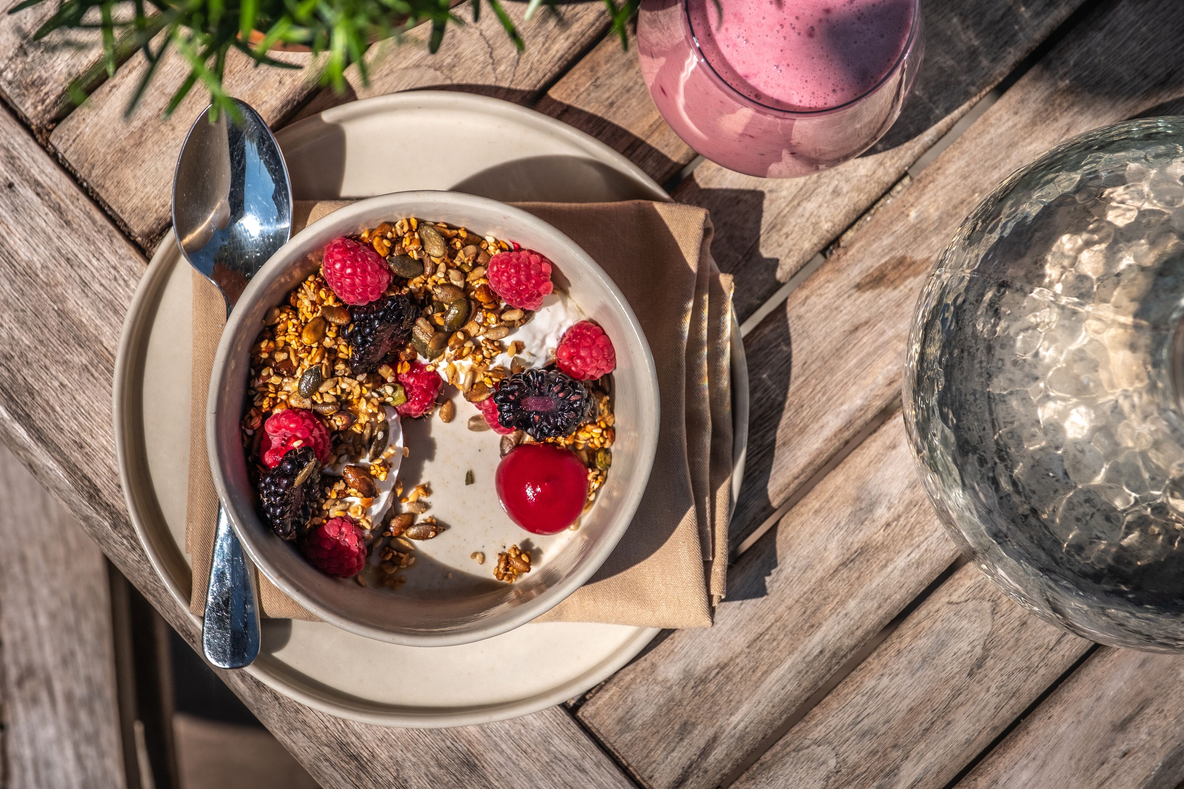 Een kom yoghurt met granola en bessen op een houten tafel.