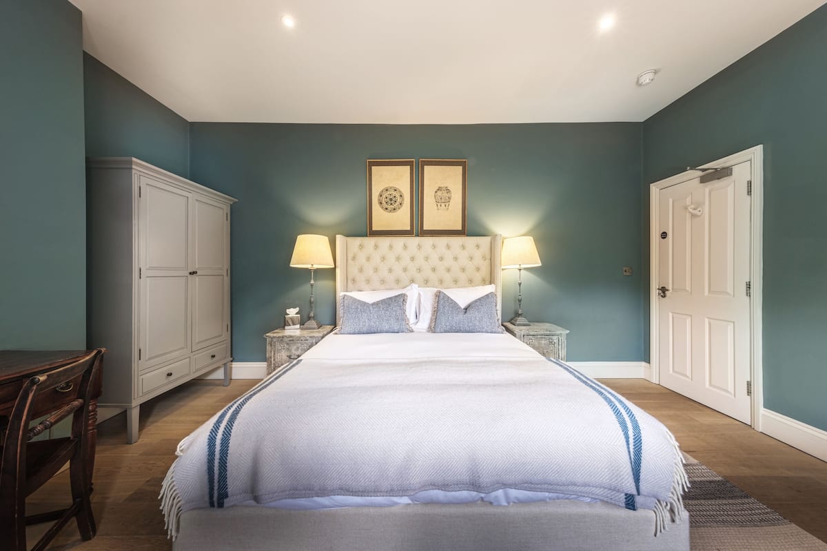 A bedroom with a large bed, two bedside tables with lamps, a wardrobe, and a door.