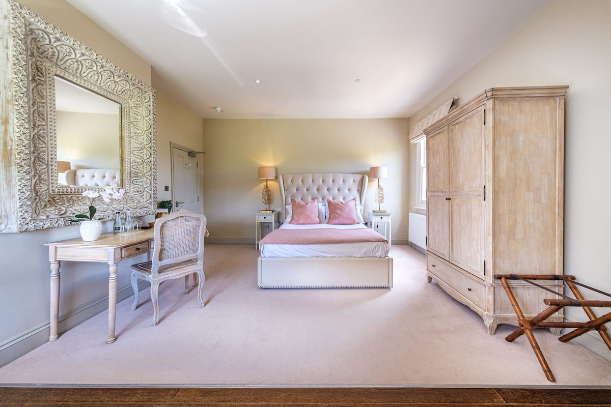 A bedroom with a large mirror, a bed with pink pillows, a desk, and a wardrobe.