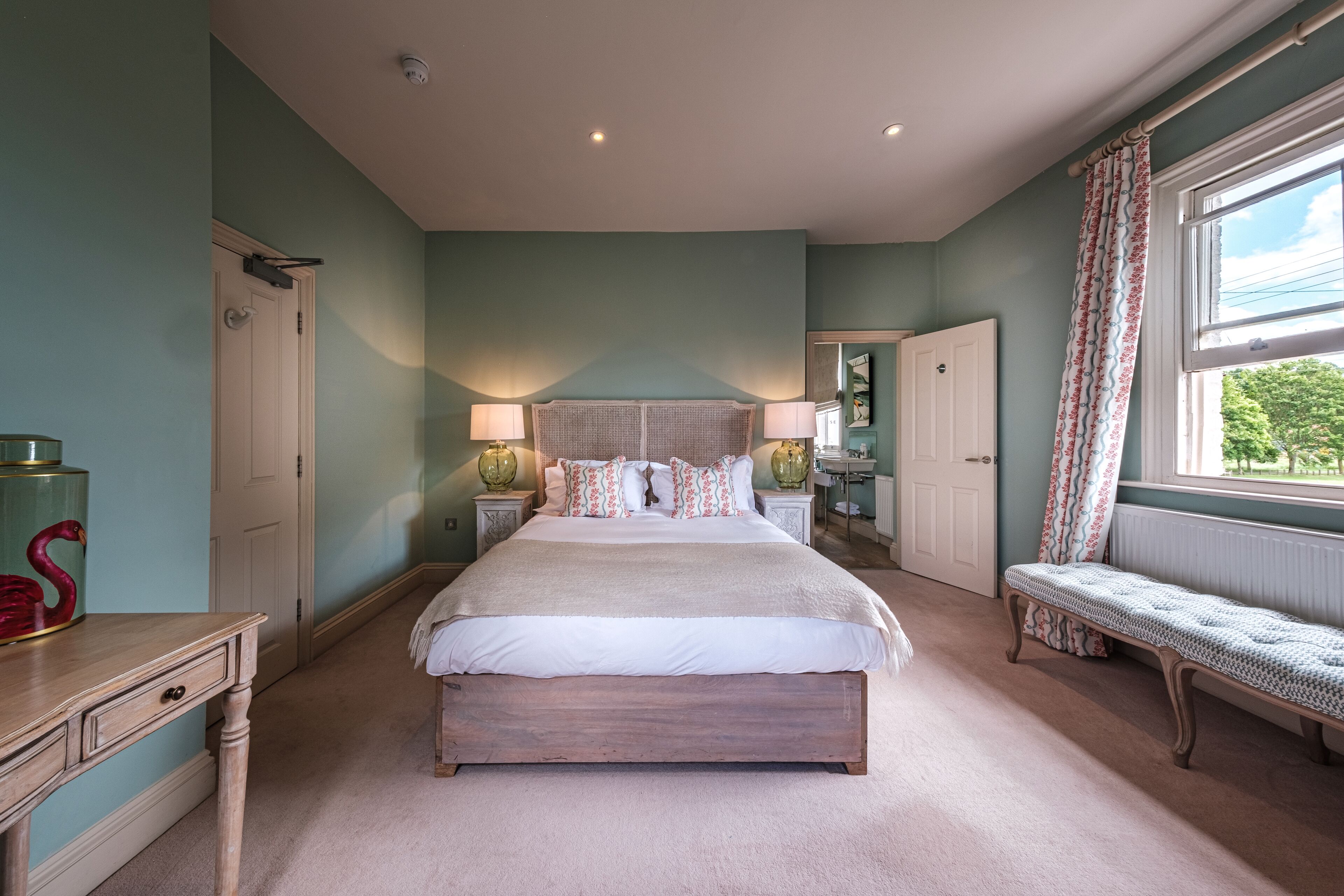A bedroom with a large bed, bedside tables, a bench, a door, and a window.