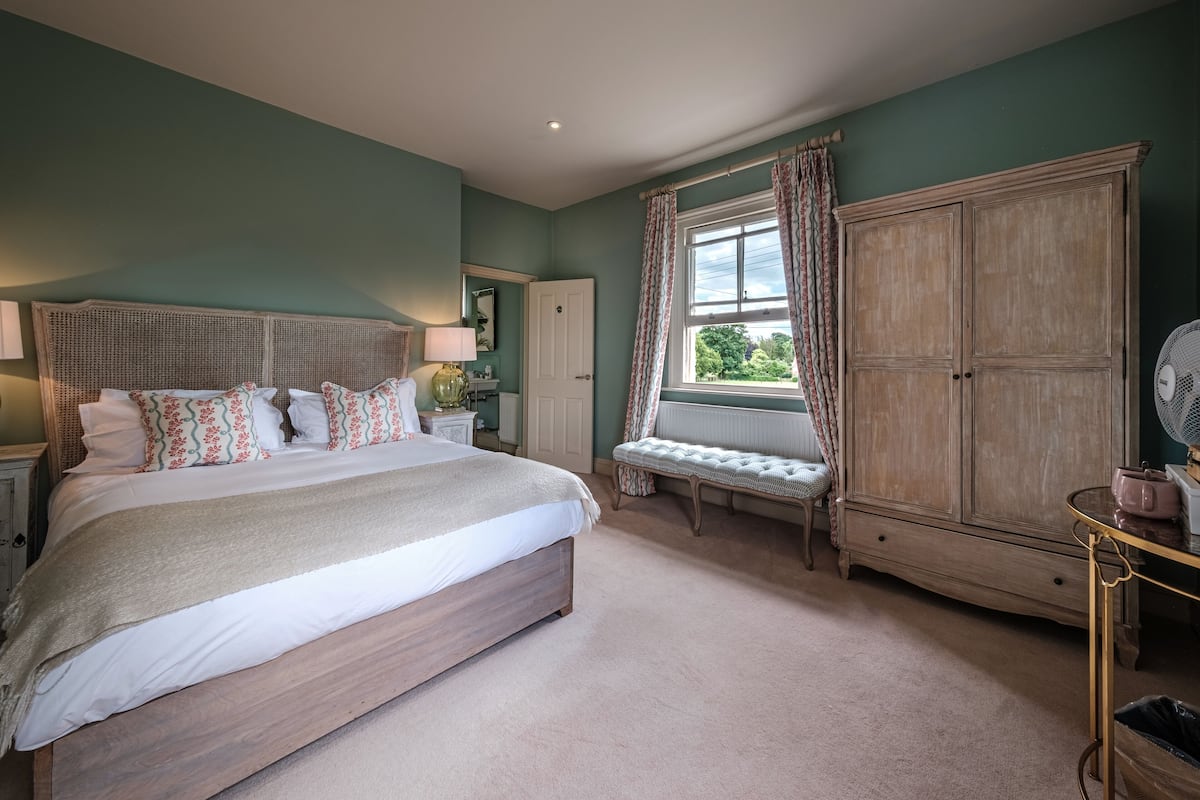 A bedroom with a large bed, a bench, a wardrobe, and a window with curtains.