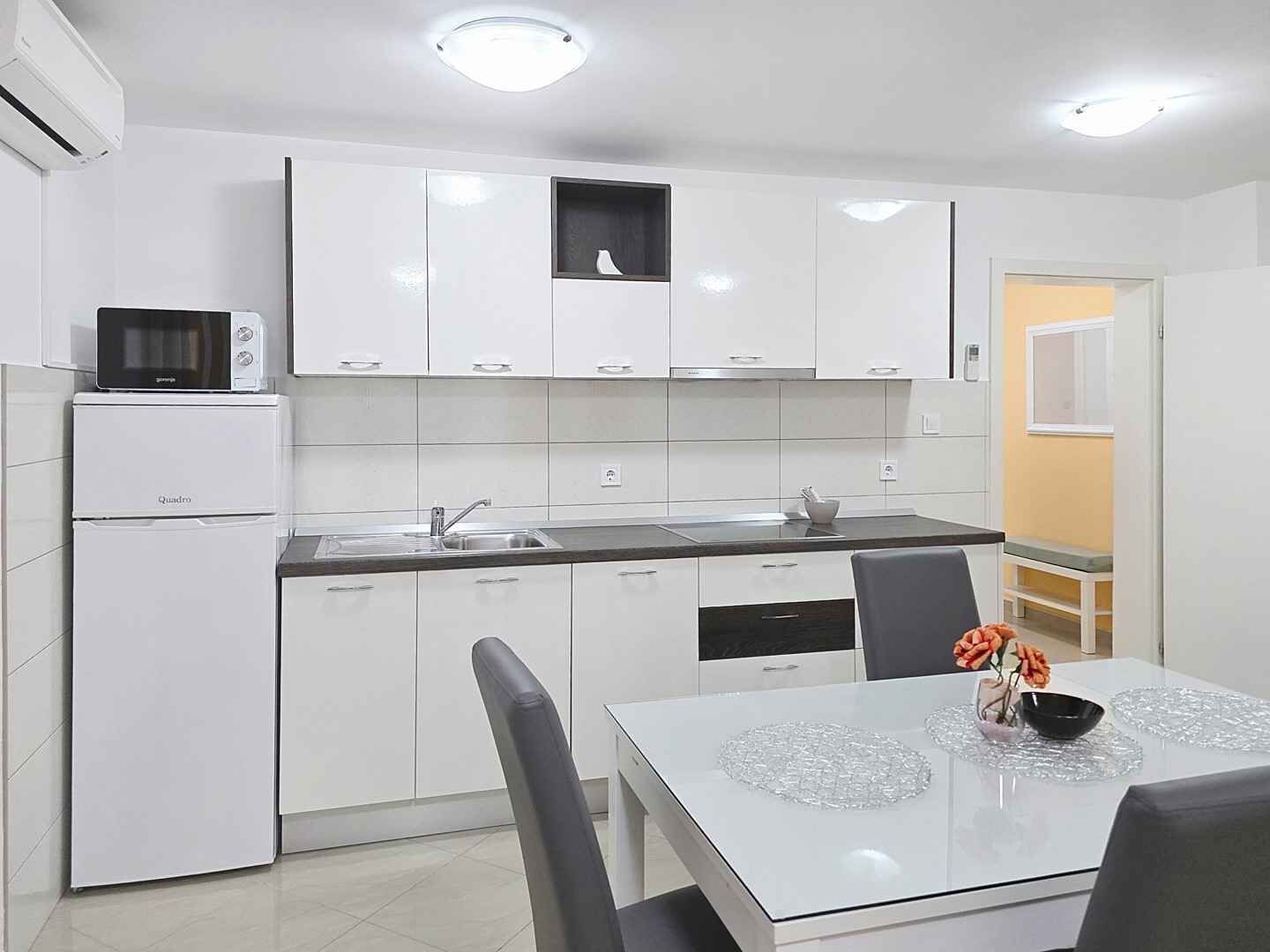 A modern kitchen with white cabinets, a microwave, a refrigerator, a sink, and a dining table with chairs.