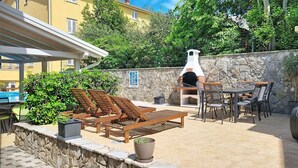 A patio with outdoor seating, a stone wall, and a pizza oven. - Holiday apartment mit Pool (Baška)
