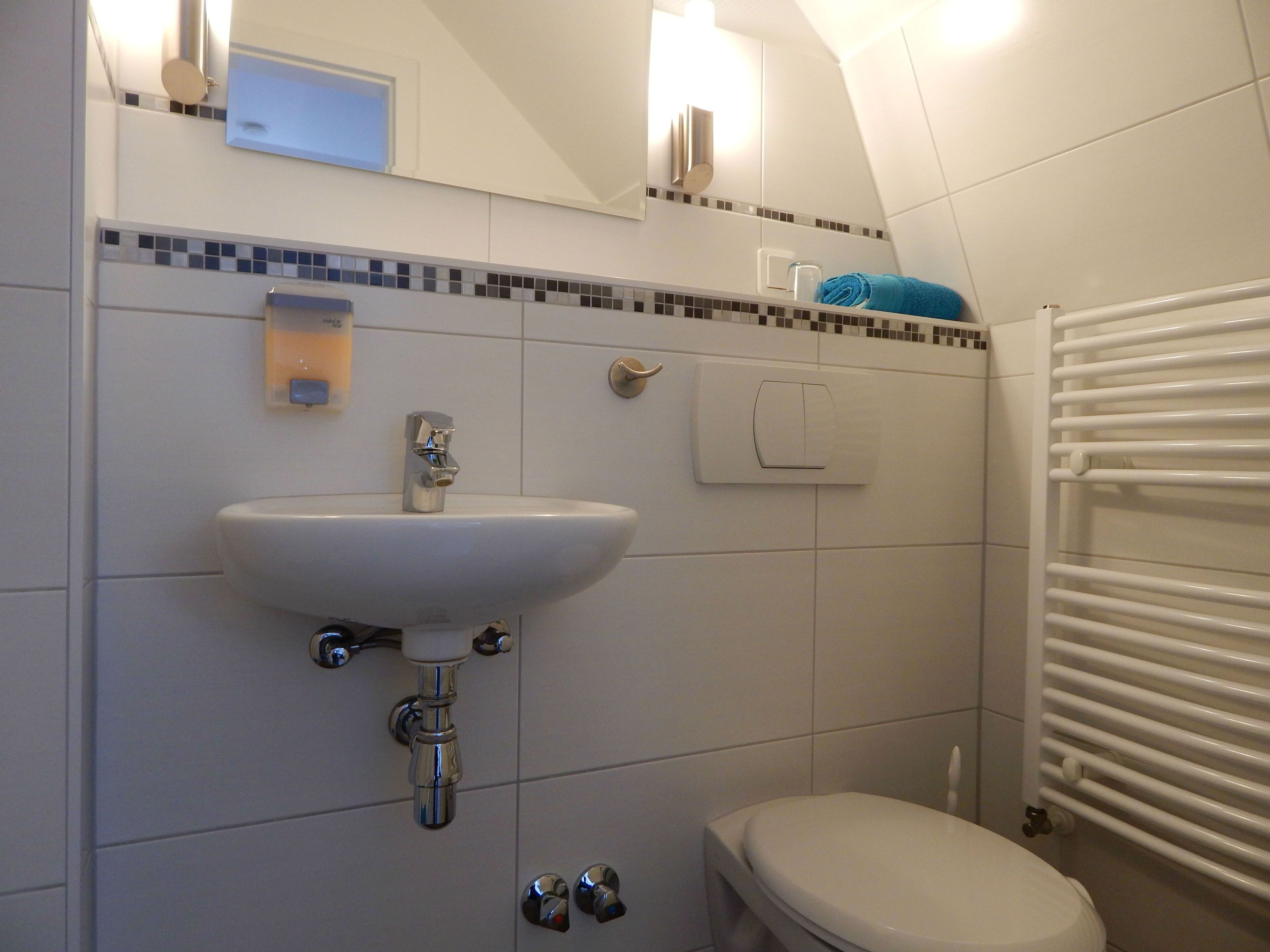 Casa de banho com lavatório branco, sanita, suporte para toalhas e radiador.
