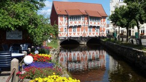 Un edificio tradicional con entramado de madera y techo rojo, un puente de piedra y un canal con flores coloridas al frente.