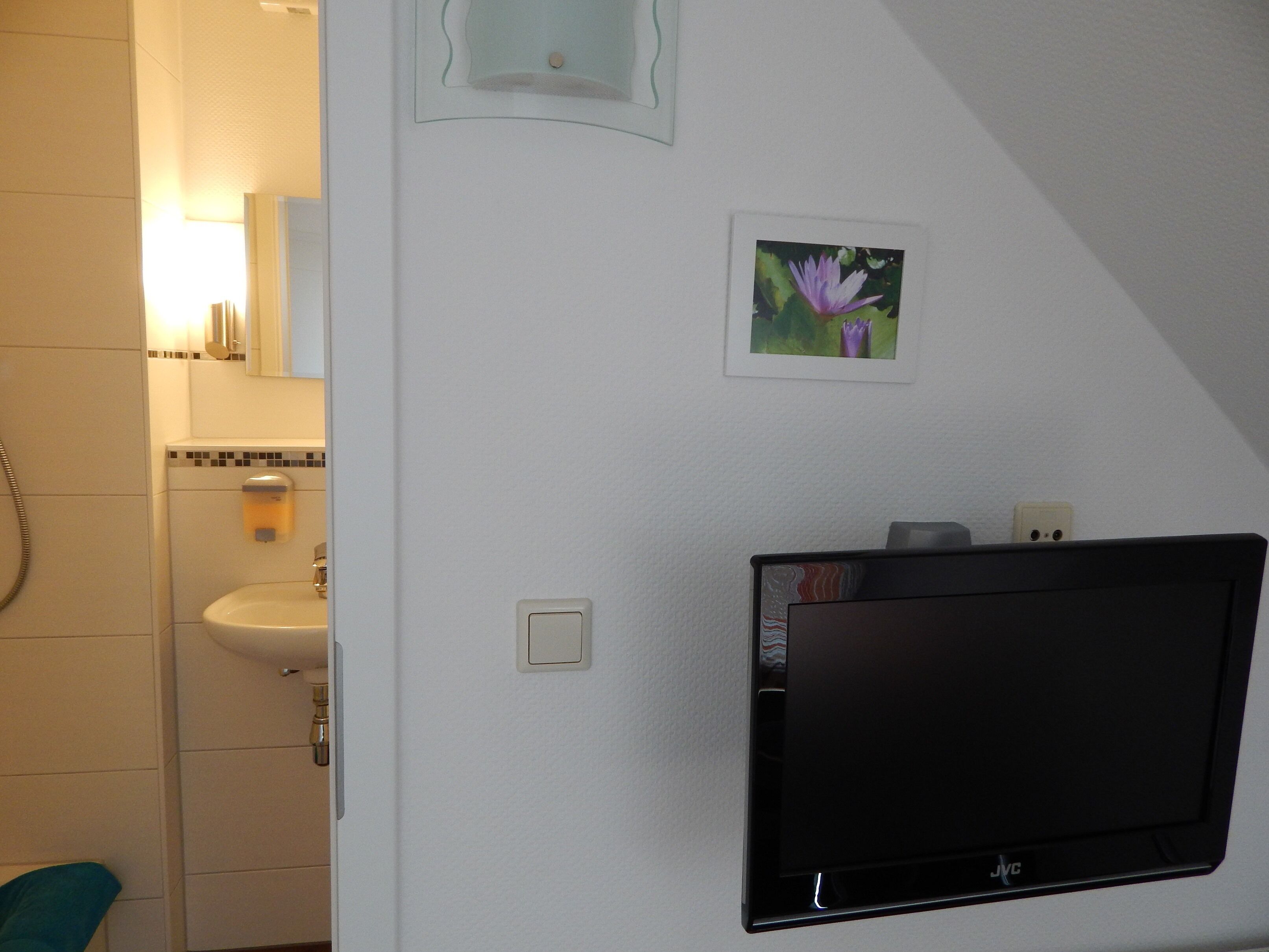 Een badkamer met een wastafel, spiegel en een aan de muur bevestigde JVC televisie.
