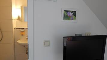 Een badkamer met een wastafel, spiegel en een aan de muur bevestigde JVC televisie.