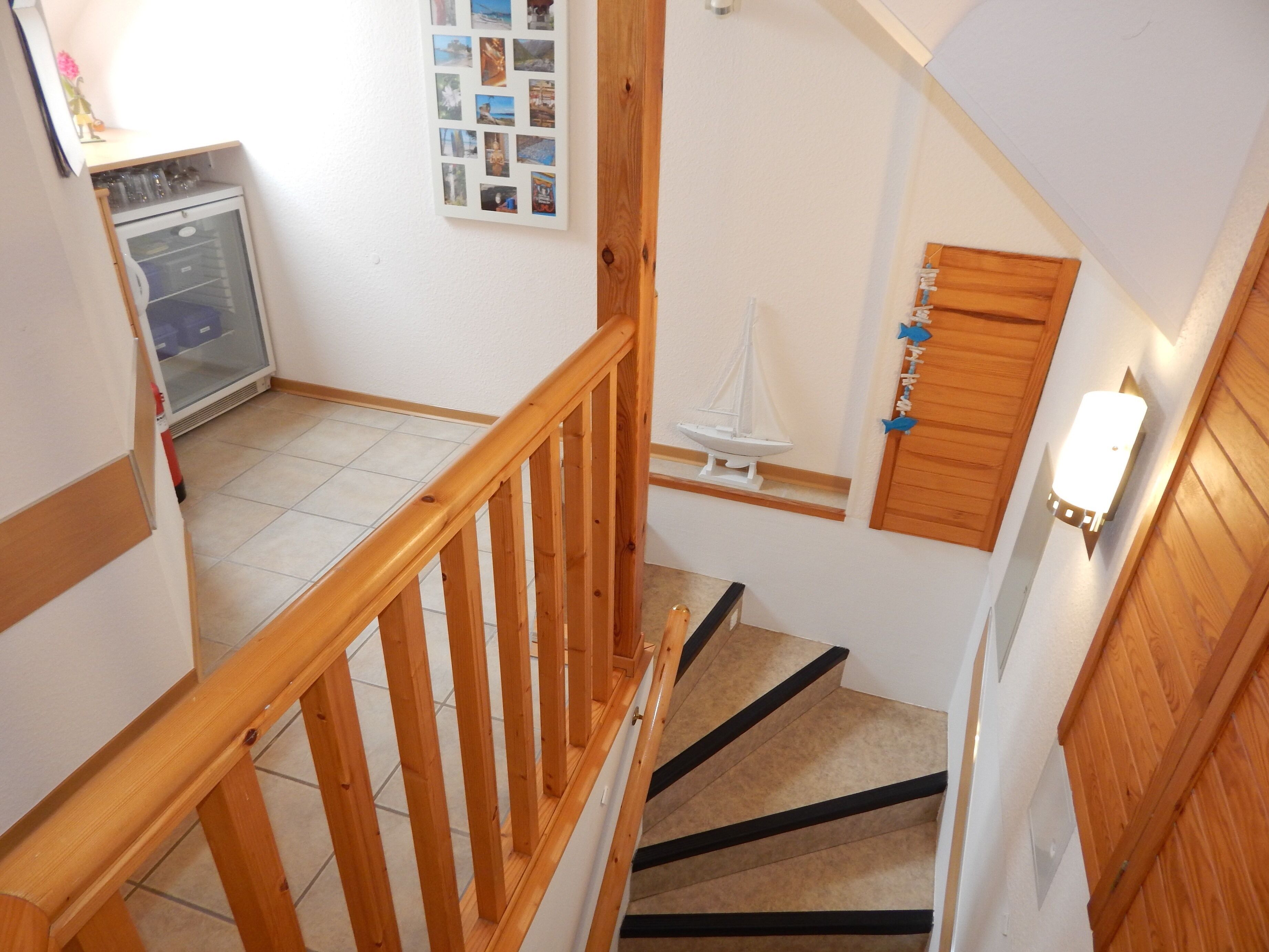 A wooden staircase with a handrail, a small sailboat decoration, and a wall-mounted light fixture.