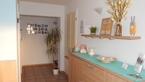 Una cocina con encimera de madera, una planta en maceta, un estante con adornos y una puerta que da a otra habitación.