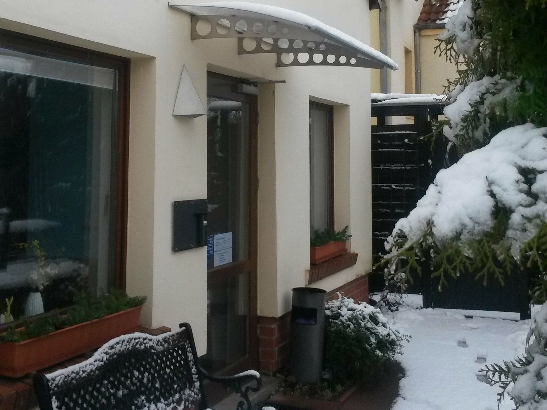 Un edificio con entrada cubierta de nieve, un banco y plantas en macetas.