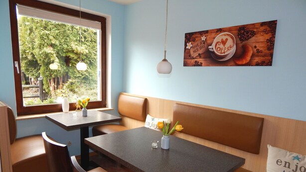 Un café acogedor con un banco de madera, dos mesas y un ventanal con vistas a zonas verdes.