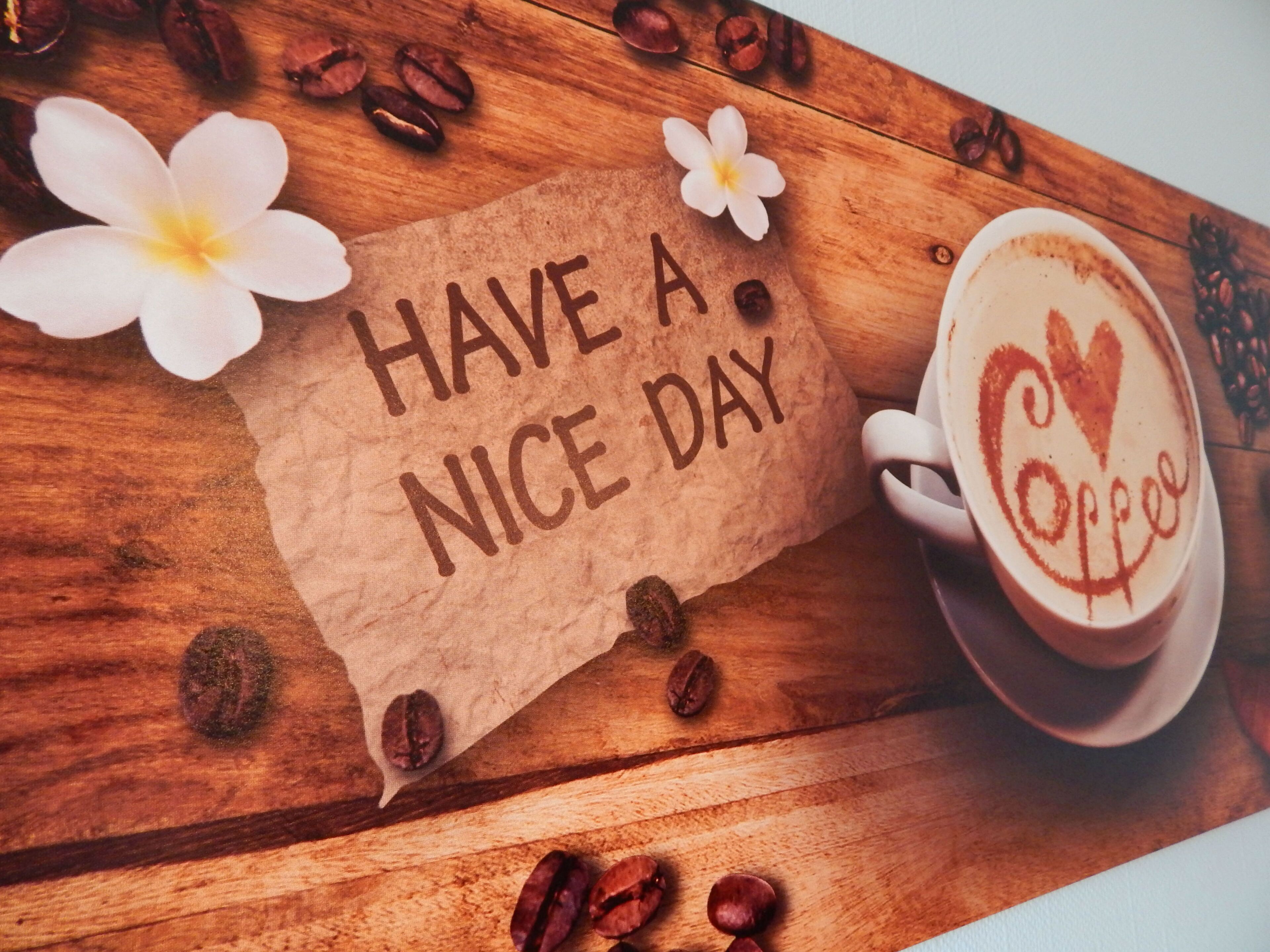 A wooden table with a coffee cup, a napkin with 'HAVE A NICE DAY' written on it, and coffee beans.