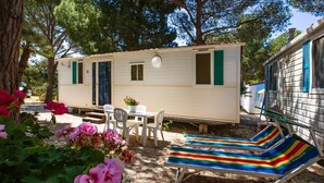 Uma casa móvel com área de varanda, incluindo uma mesa e cadeiras, e uma cadeira de descanso listrada e colorida.