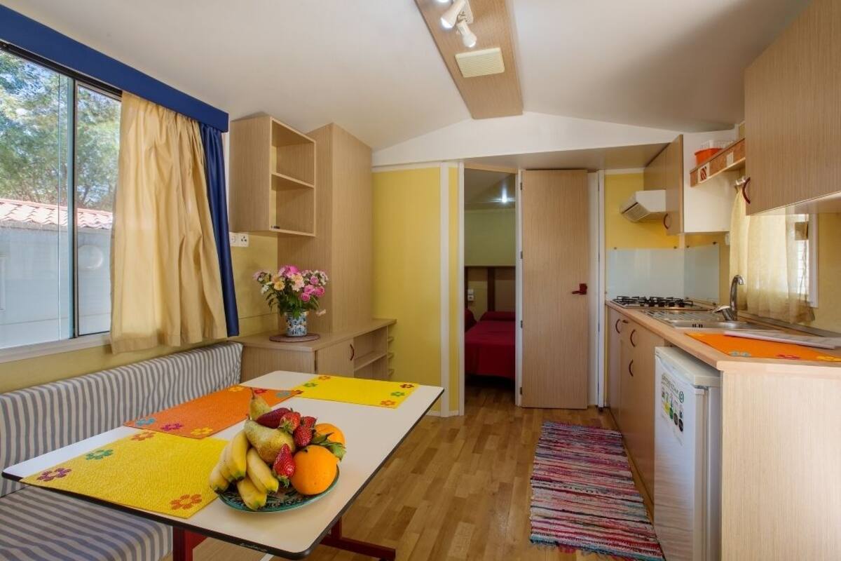 Eine kleine Küche mit Essbereich, einem Kühlschrank und einem Fenster mit Vorhängen.