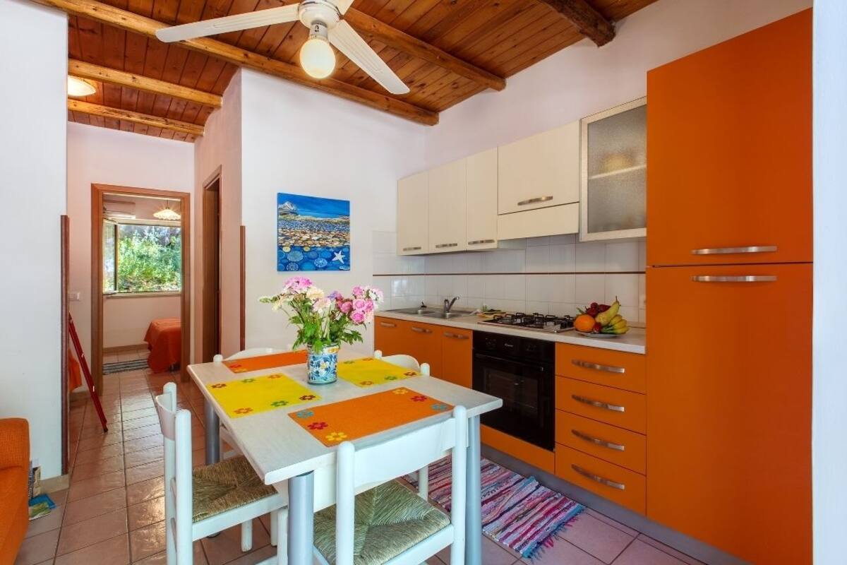 Eine Küche mit weißen Schränken, einem orangefarbenen Kühlschrank und einem Essbereich mit Tisch und Stühlen.