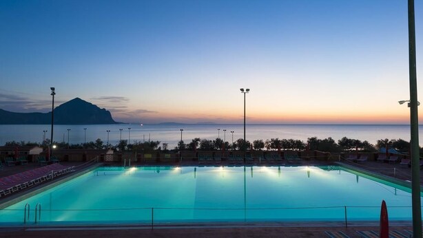Piscina com vista para o mar e uma montanha ao pôr do sol.