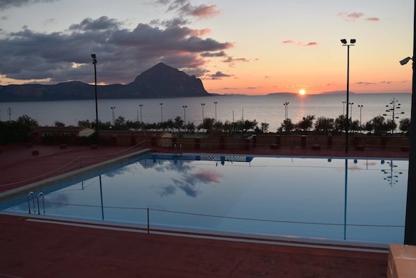 A swimming pool with a sunset view, surrounded by a red deck and street lamps. - Camping Village El-Bahira (San Vito Lo Capo)