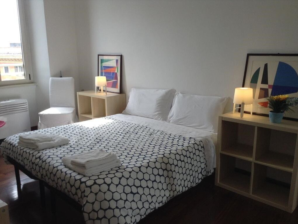 Habitació d'hotel amb un llit, taules de nit, una làmpada, un quadre amb marc i una finestra.