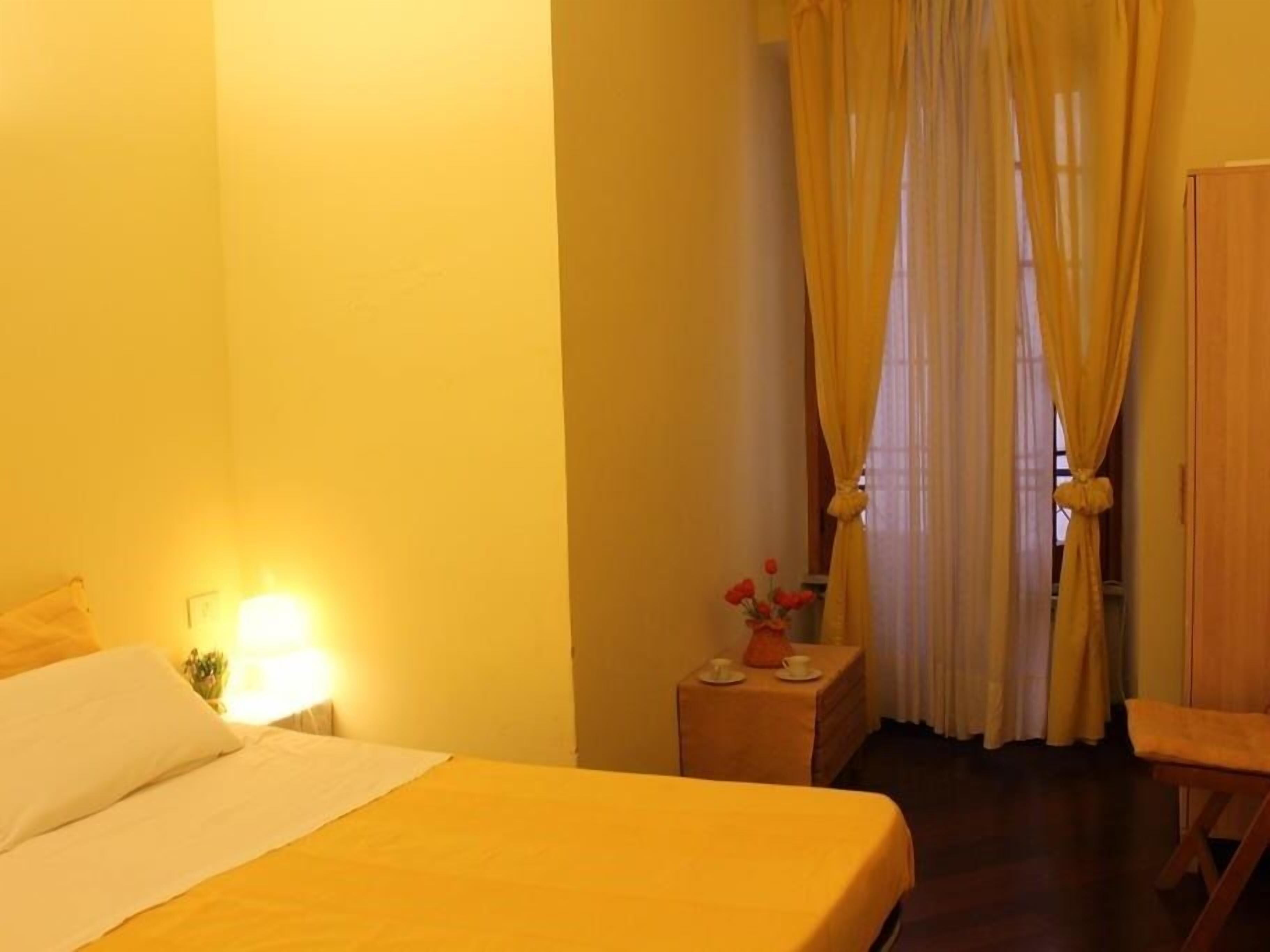 Quarto de hotel com cama, mesa de cabeceira, uma mesa com um vaso de flores e uma cadeira.