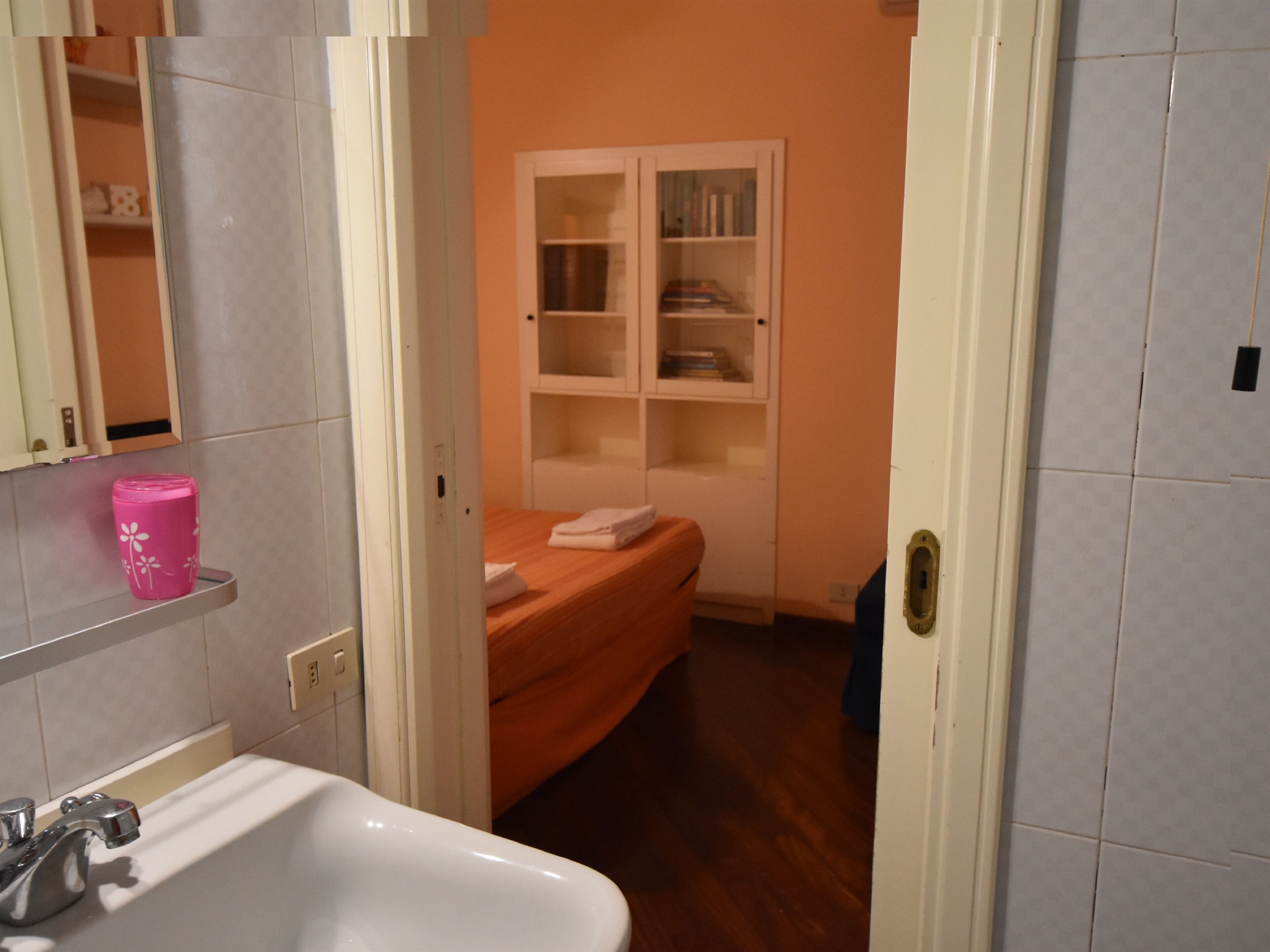 A bathroom with a white sink, a pink vase, and a wooden bench.