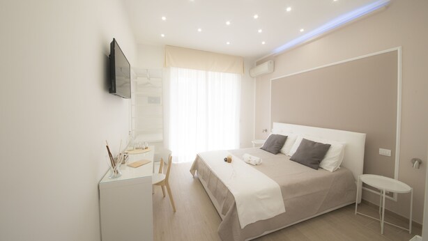 A modern hotel room with a large bed, a desk with a chair, a TV mounted on the wall, and a window with curtains. - B&B Chérie - Centro di Salerno (Salerno)