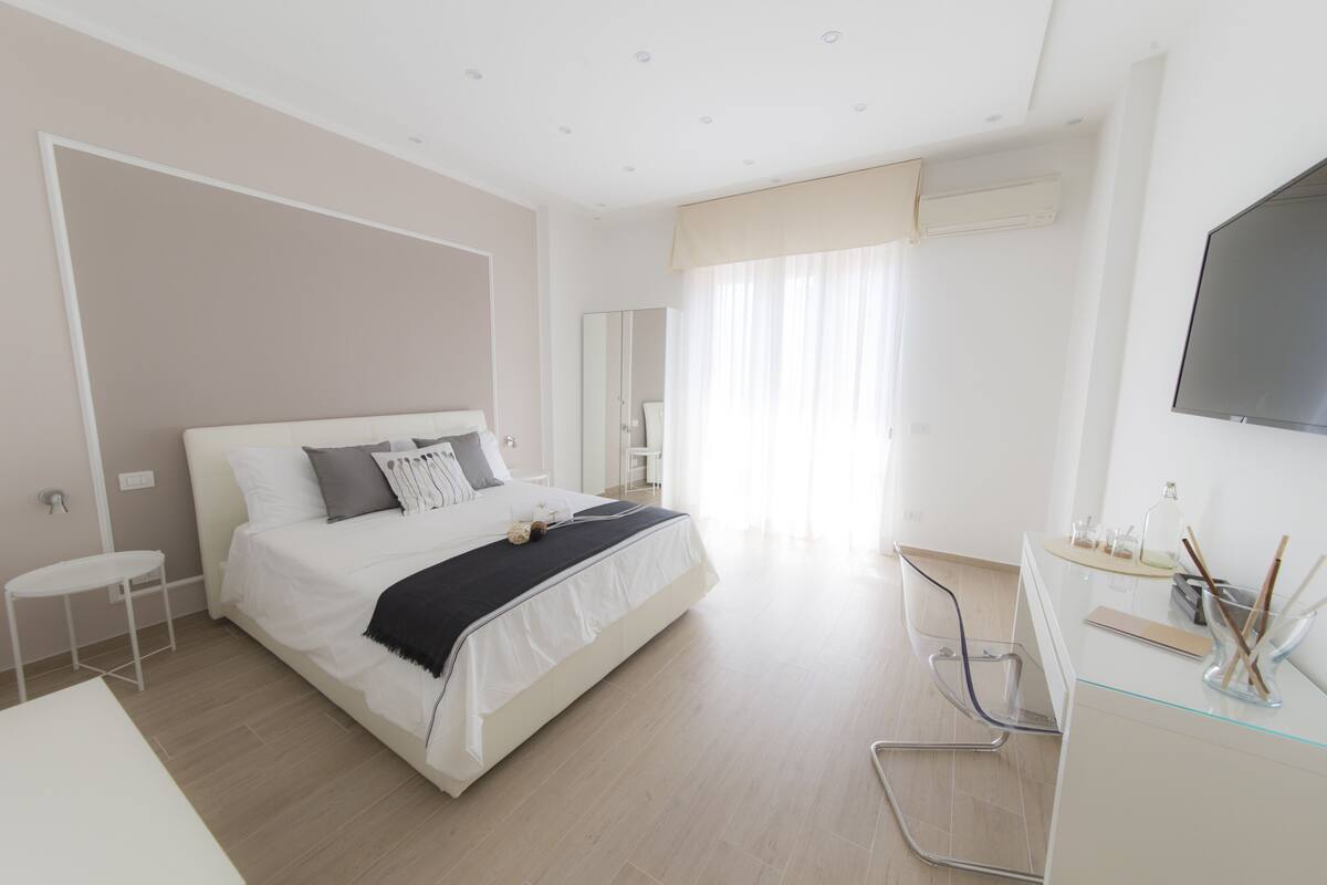 A modern bedroom with a large bed, a desk, and a TV.