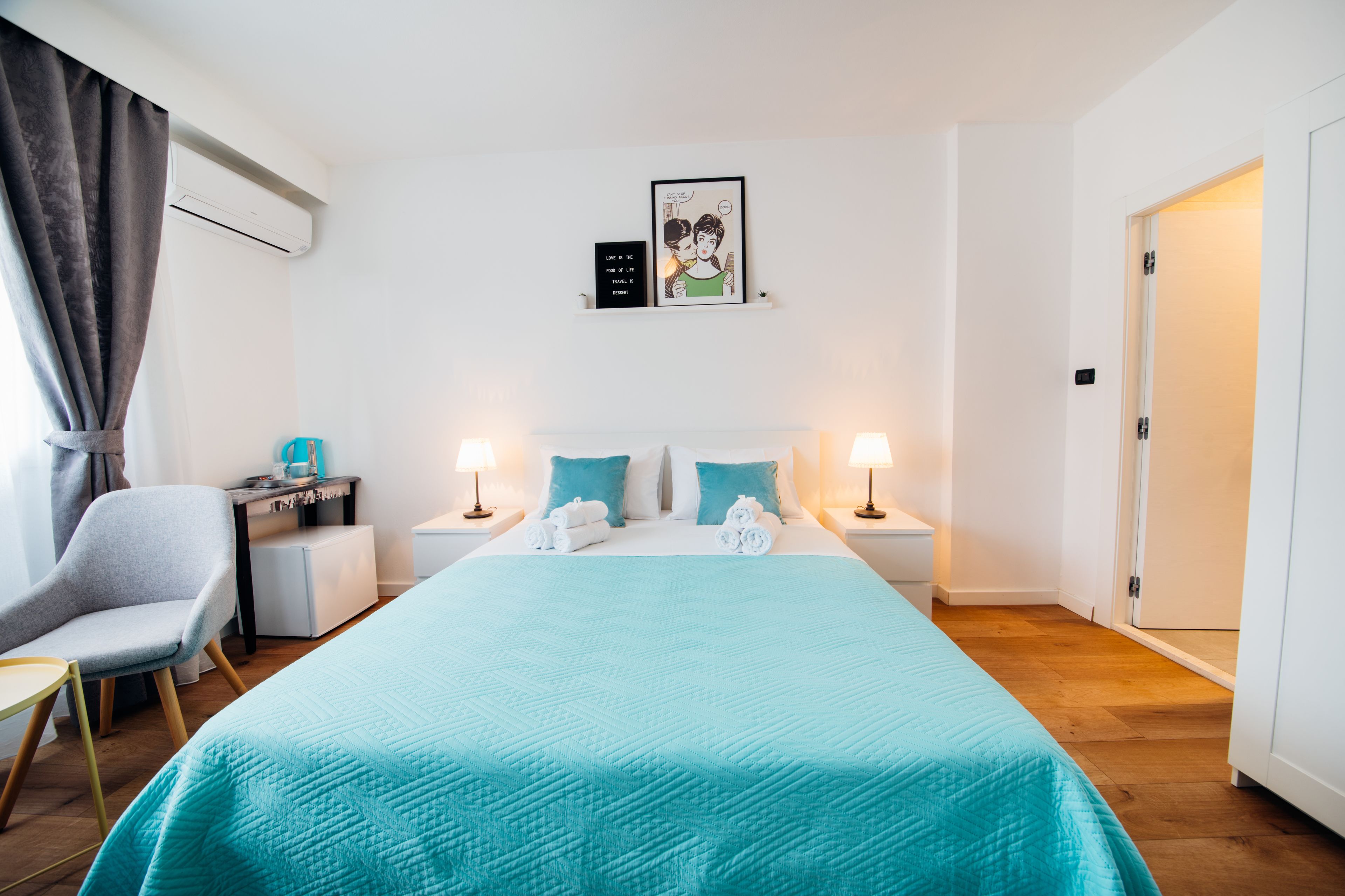 Une chambre d’hôtel avec un grand lit, deux tables de chevet avec des lampes, un bureau avec une chaise et une porte.