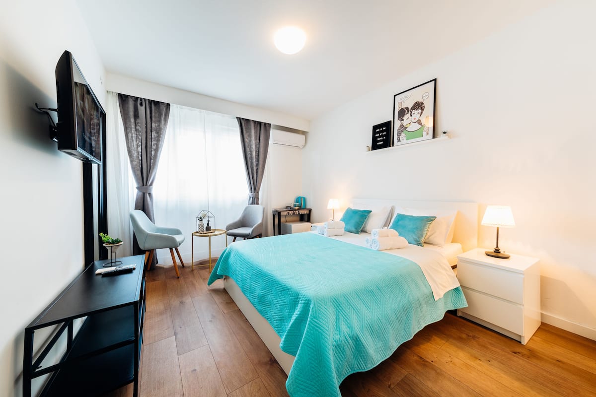 Et moderne hotelværelse med seng, sengebord, TV og skrivebord med stol.