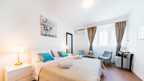 A hotel room with a bed, bedside table, lamp, chair, desk, and artwork. - The Harmony Rooms Split (Split)