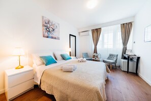 A hotel room with a bed, bedside table, lamp, chair, desk, and artwork. - The Harmony Rooms Split (Split)