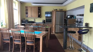 A modern kitchen with wooden cabinets, a stainless steel refrigerator, and a dining area with wooden chairs and a table. - Families, groups, cycling, biking, hiking, vacation with dog, short vacation, Kyllradweg, (Stadtkyll)