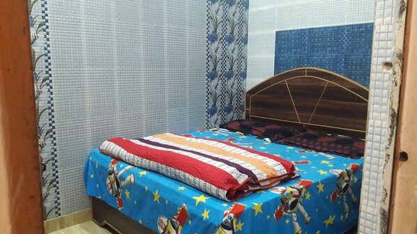 Un dormitorio con una cama cubierta por un edredón colorido, cabecera de madera y cortinas estampadas.