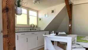 Una cocina compacta con armarios blancos, una mesa de comedor blanca y una sola silla blanca.