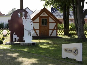 Entrada a un parque con una estatua blanca de un hombre sosteniendo una bombilla, la silueta de un gato y un letrero que dice "Parkplatz L".