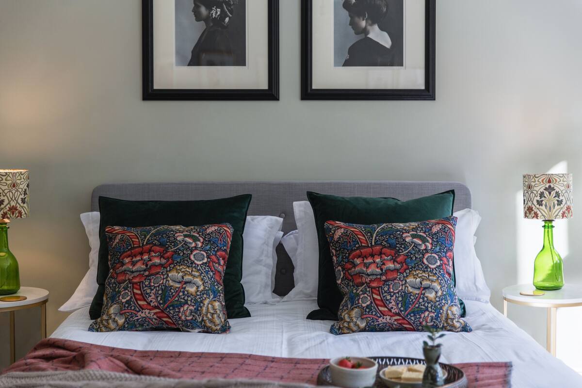A neatly made bed with patterned pillows, a bedside table with a lamp, and framed pictures on the wall.