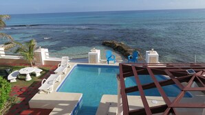 Una piscina con agua azul cristalina, rodeada de sillones de descanso y vista al océano.