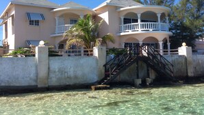 Una propiedad frente al mar de dos pisos con un balcón y una escalera que lleva al nivel superior, con vista despejada al océano.