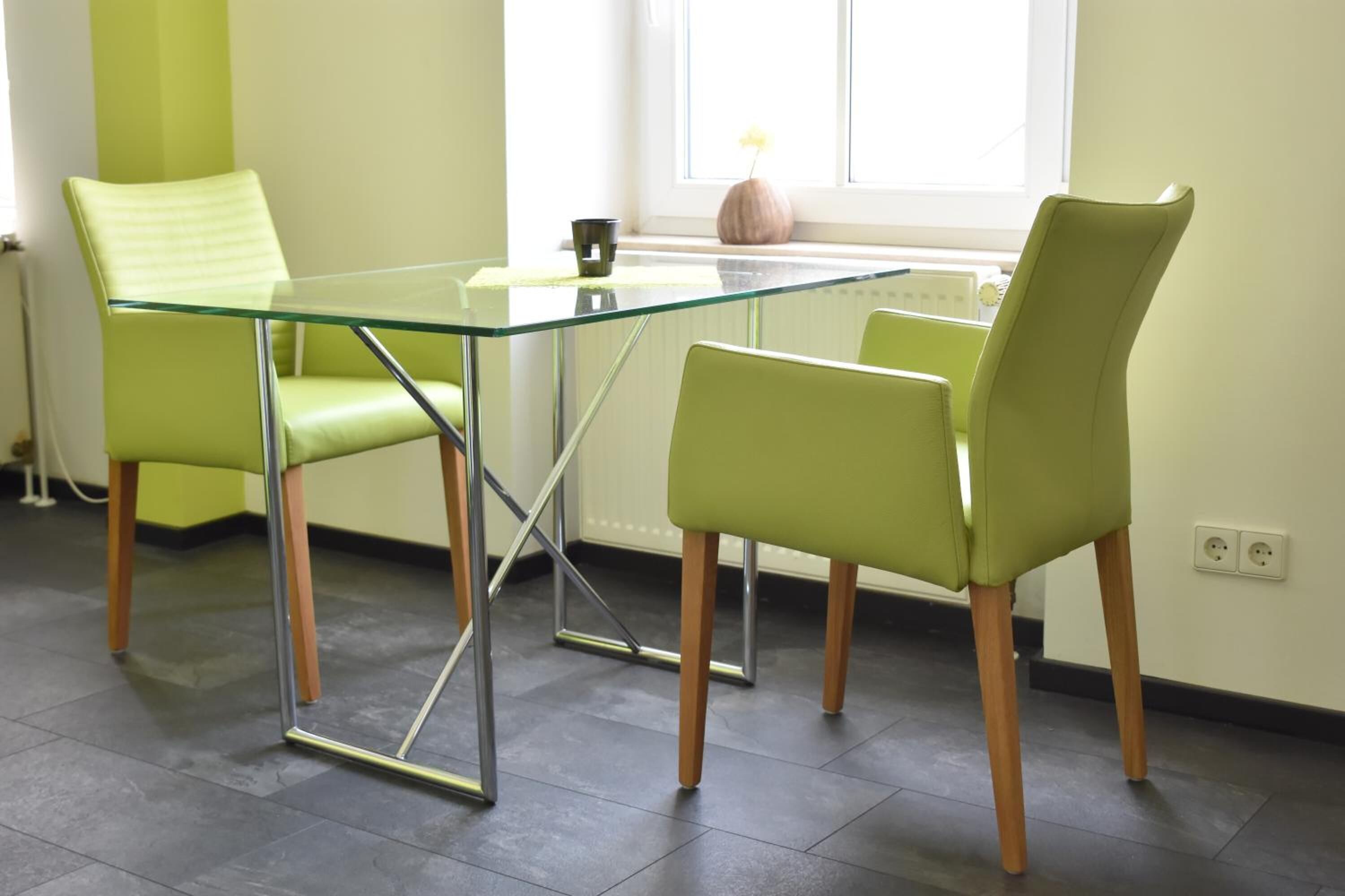 A modern dining area with a glass table and two green chairs.