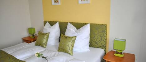 A neatly made bed with white and green bedding, two bedside tables with green lamps, and two framed pictures on the wall.