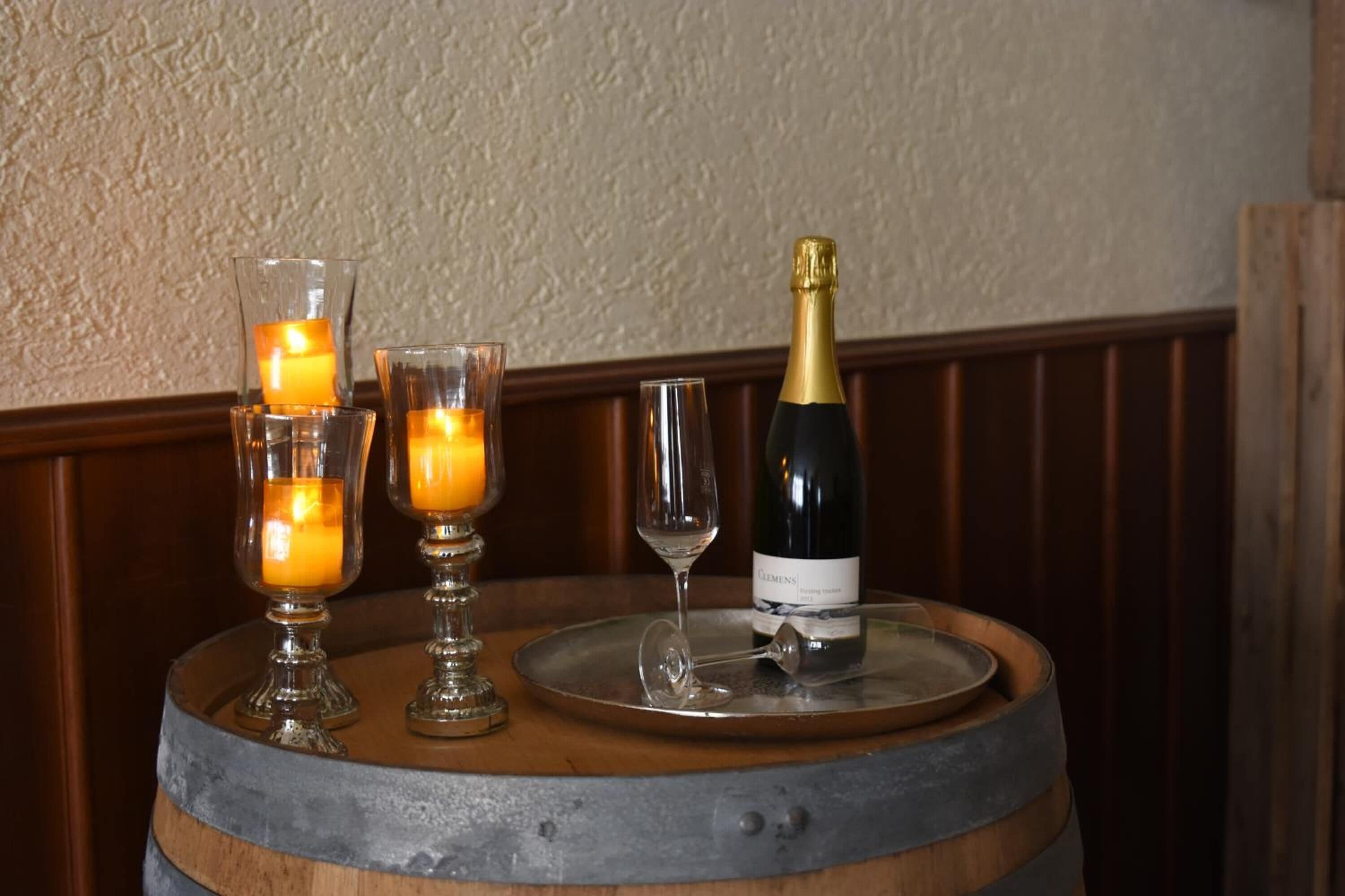 A wooden barrel table with a bottle of champagne, two candle holders with candles, and a wine glass.