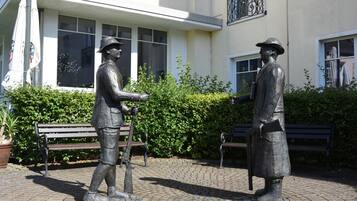 Een standbeeld van twee figuren in een binnenplaats met banken en een gebouw op de achtergrond.