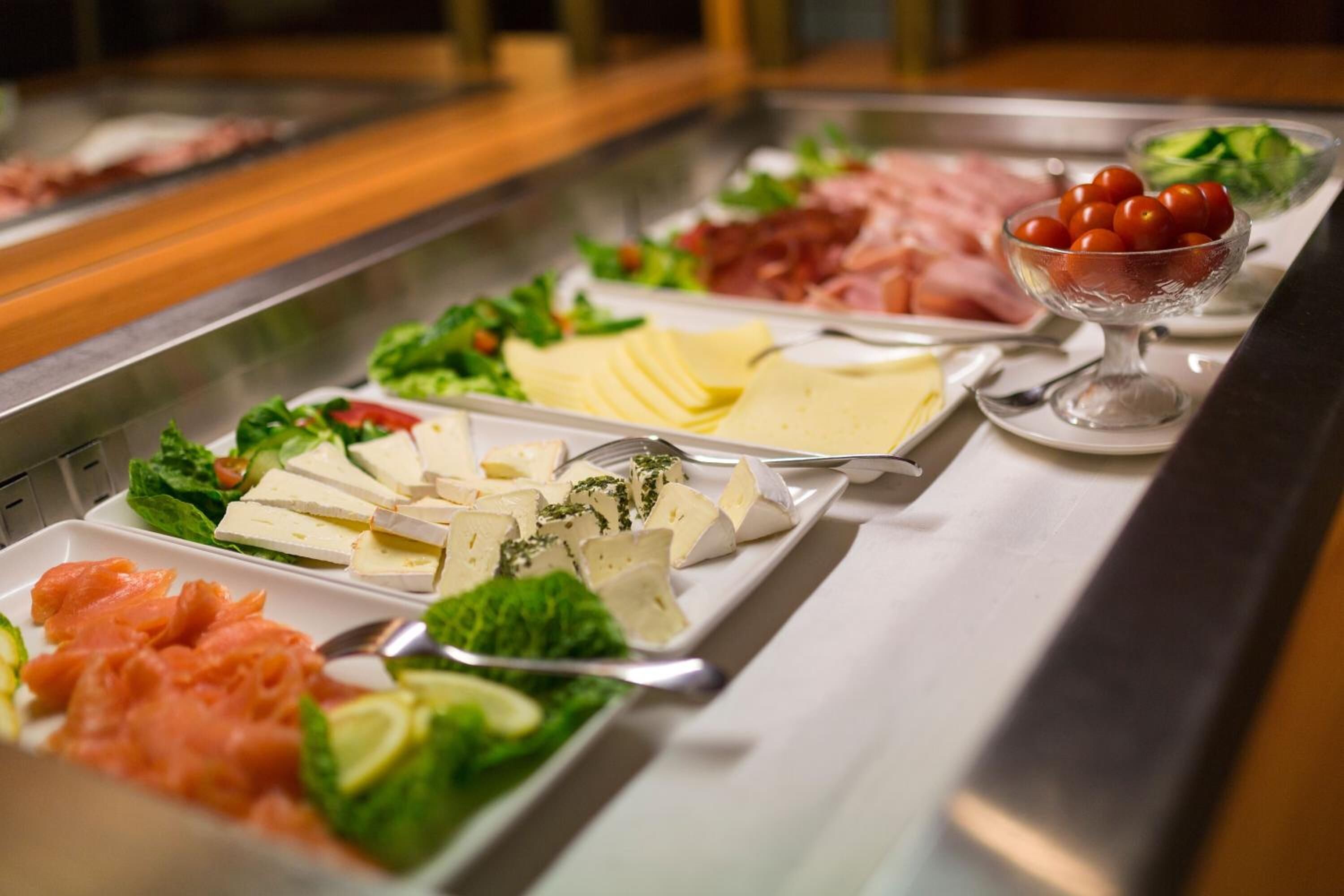 A buffet with various cheeses, meats, and vegetables.