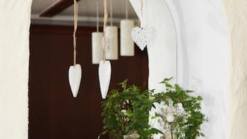 A rustic interior with a white arched window, a potted plant, a decorative sheep sculpture, and hanging heart-shaped ornaments.